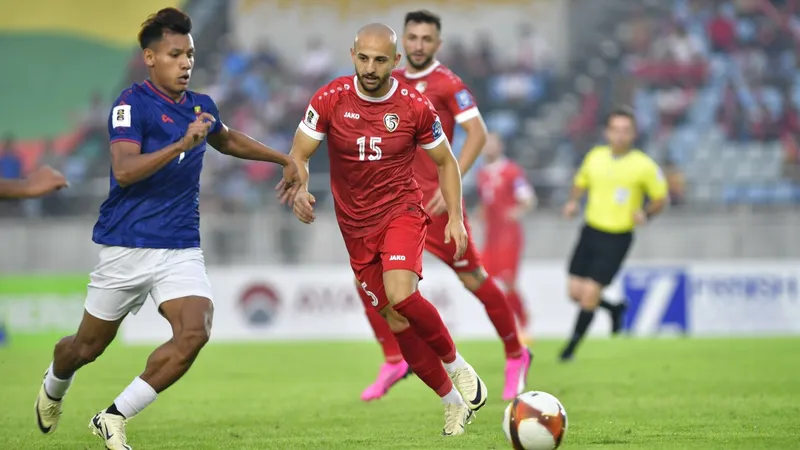Cầu thủ Myanmar đi bóng qua cầu thủ Syria trong trận đấu bóng đá quốc tế